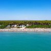 Vista aerea di una spiaggia affollata con mare azzurro e foresta alle spalle.