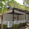 Una casa mobile con veranda, circondata da cespugli e alberi, sotto la luce del sole.