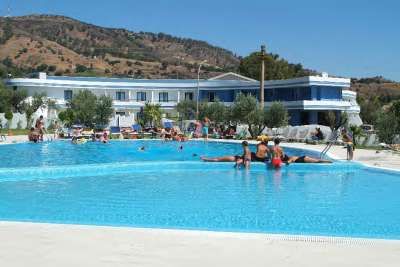 Una grande piscina all'aperto con persone che nuotano e un edificio bianco e blu sullo sfondo.