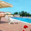 Piscina all'aperto con lettini e ombrelloni, circondata da sedie in vimini e piante.