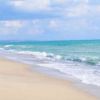 Una spiaggia sabbiosa con onde che si infrangono dolcemente e un cielo nuvoloso.