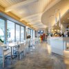 Interno di un bar moderno con tavoli bianchi e pareti finestrate.