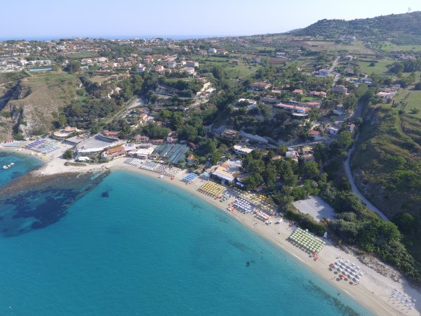 Vista aerea di una spiaggia con mare blu e colline verdi.