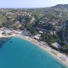 Vista aerea di una spiaggia con mare blu e colline verdi.